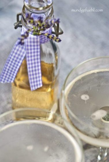 Zwei Gläser mit Prosecco und Lavendelsirup stehen vor einer Glasflasche
