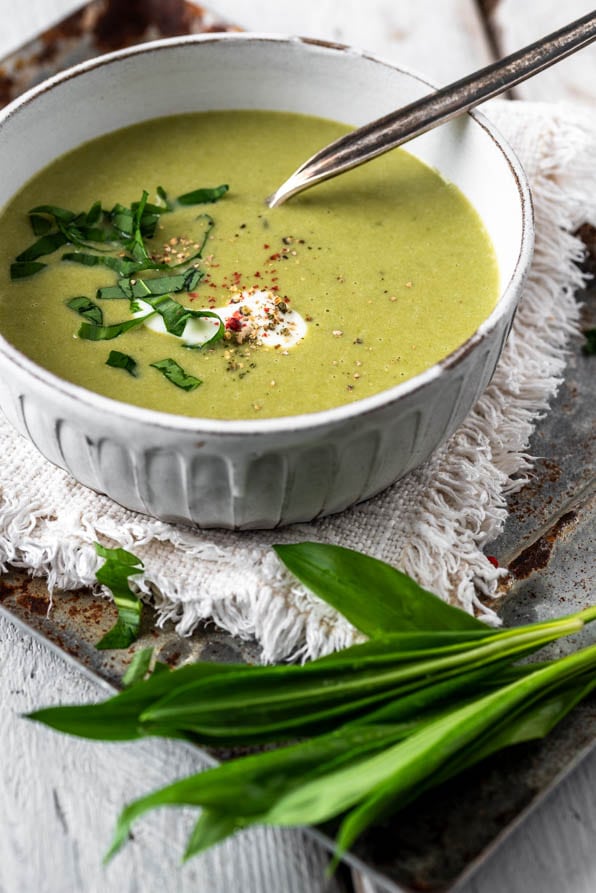 Cremige Bärlauchsuppe in heller Schale, mit Sahnetupfer, Gewürzen und frischem Bärlauch