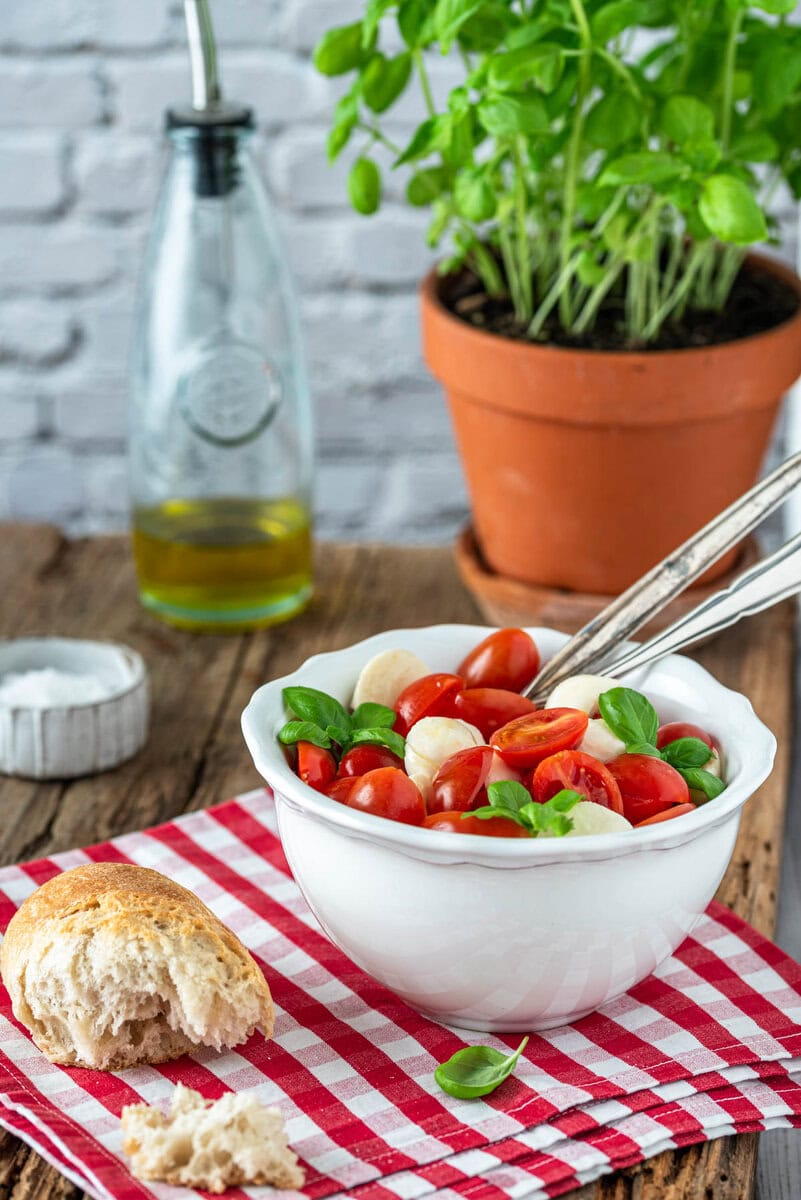Ein Schälchen Tomaten Mozzarella Salat mit Baguette und Basilikumstrauch