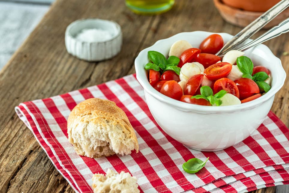 Ein Schälchen Tomaten Mozzarella Salat mit Baguette und Basilikumstrauch
