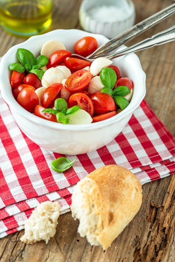Ein Schälchen Tomaten Mozzarella Salat mit Baguette und Basilikumstrauch
