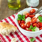 Ein Schälchen Tomaten Mozzarella Salat mit Baguette und Basilikumstrauch