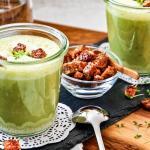 Zwei Gläser mit Erbsensuppe und einem Schälchen Croutons stehen auf einem Holzbrett