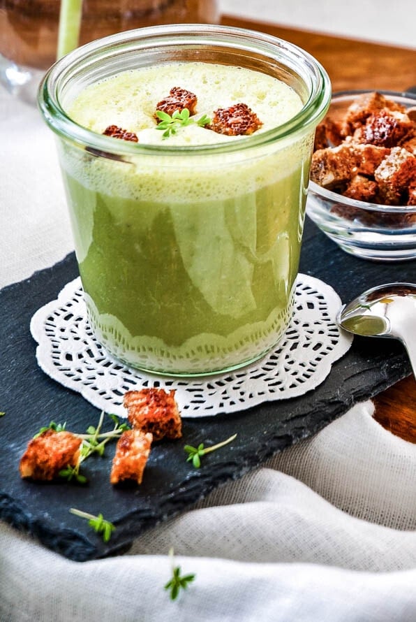 Zwei Gläser mit Erbsensuppe und einem Schälchen Croutons stehen auf einem Holzbrett