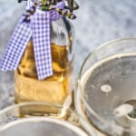 Zwei Gläser mit Prosecco und Lavendelsirup stehen vor einer Glasflasche