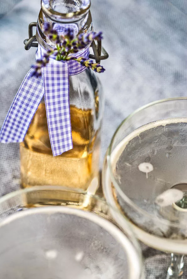 Zwei Gläser mit Prosecco und Lavendelsirup stehen vor einer Glasflasche