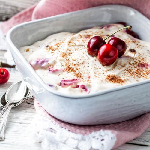 Tiramisu mit Kirschen in einer Form auf einem weißen Untergrund.