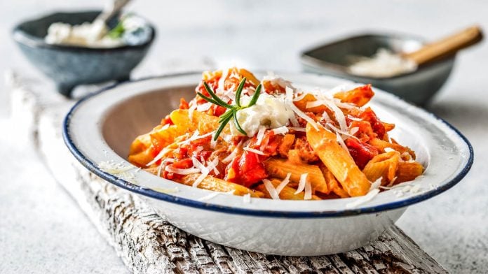 Teller mit Penne mit Tomaten und Ricotta Sauce auf einem Holzbrett