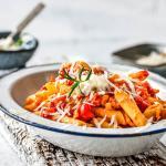 Teller mit Penne mit Tomaten und Ricotta Sauce auf einem Holzbrett