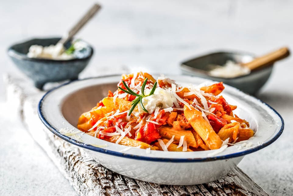 Teller mit Penne mit Tomaten und Ricotta Sauce auf einem Holzbrett