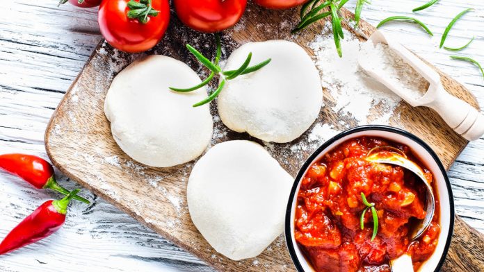 pizzateig-selber-machen 3 Kugeln Pizzateig liegen auf einem Brett neben Tomaten und einer Schüssel Tomatensauce