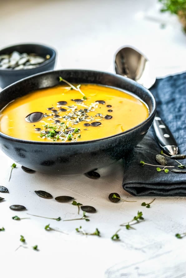 Schüssel mit Kürbissuppe ist mit Kürbiskernen und Kresse garniert