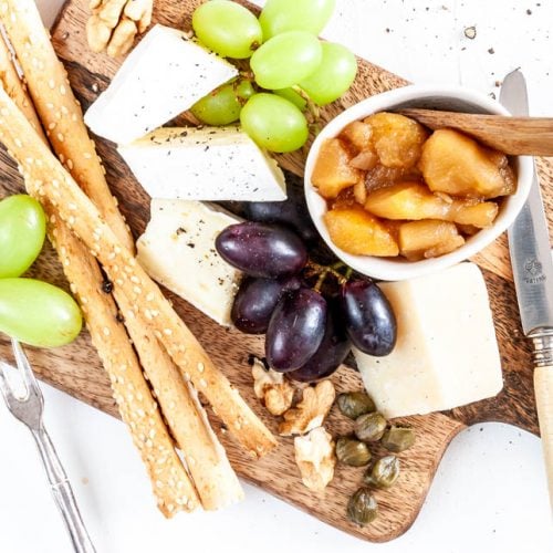 Käseplatte garniert mit Apfelchutney, Weintrauben und Grissini