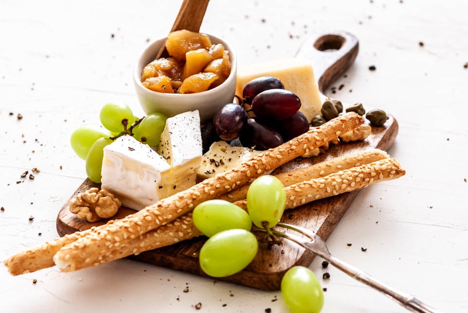 Käseplatte garniert mit Apfelchutney, Weintrauben und Grissini