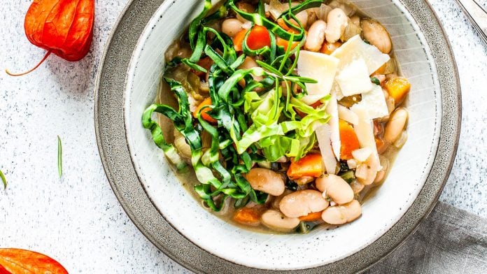 Bohnensuppe in einem Teller steht vor einem Topf mit Suppe.