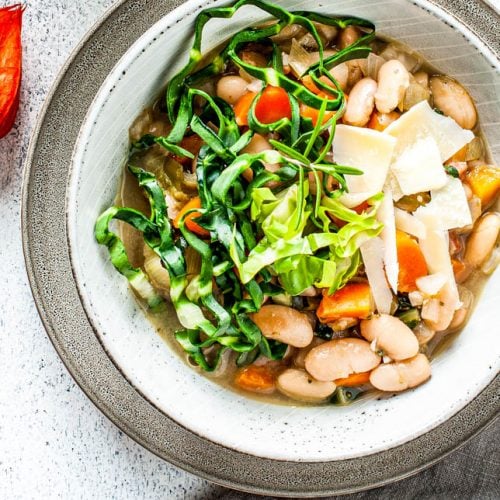 Bohnensuppe in einem Teller steht vor einem Topf mit Suppe.