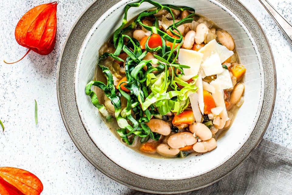 Bohnensuppe in einem Teller steht vor einem Topf mit Suppe.