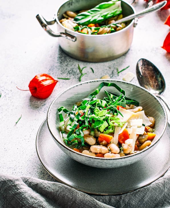 Bohnensuppe in einem Teller steht vor einem Topf mit Suppe.