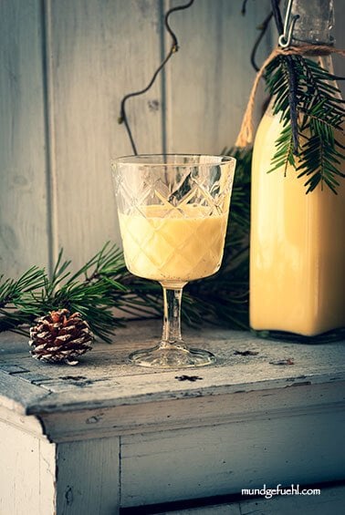 Ein Glas und eine Flasche Eierlikör stehen auf einem Kästchen mit weihnachtlicher Deko