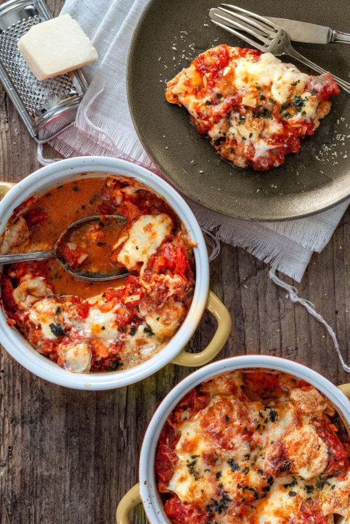 Mit Tomaten und Mozzarella überbackenes Huhn wird von feuerfester Form auf Teller angerichtet