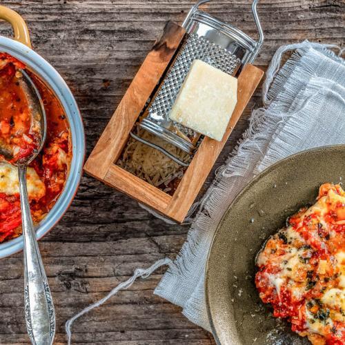 Mit Tomaten und Mozzarella überbackenes Huhn wird von feuerfester Form auf Teller angerichtet