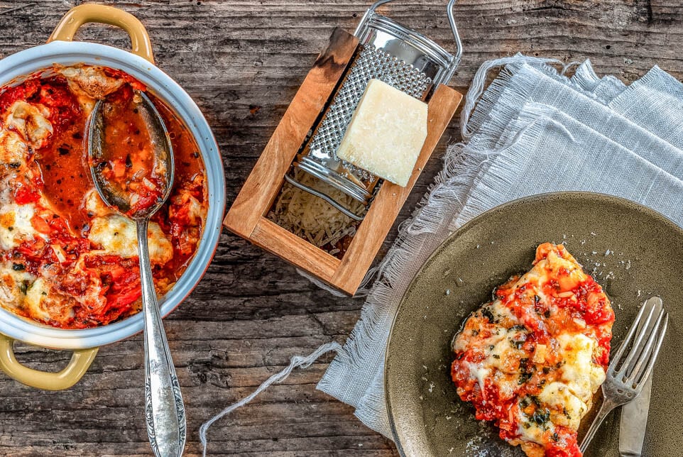 Mit Tomaten und Mozzarella überbackenes Huhn wird von feuerfester Form auf Teller angerichtet