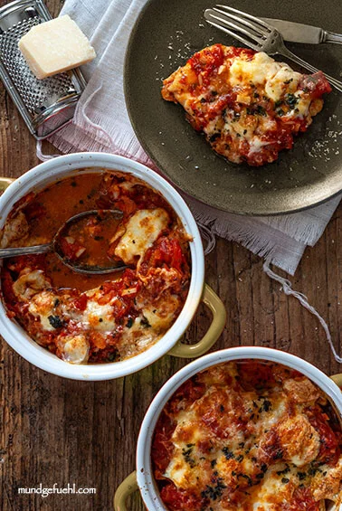 Chicken gratinated with tomatoes and mozzarella is served from an ovenproof dish onto plates