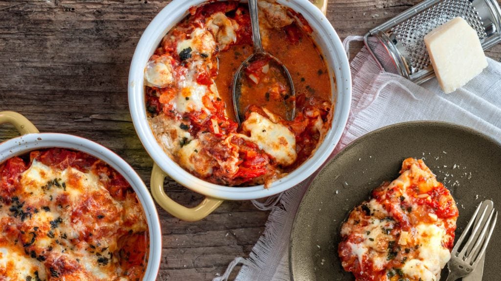 Mit Tomaten und Mozzarella überbackenes Huhn wird von feuerfester Form auf Teller angerichtet