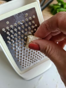 Hand reibt Parmesan auf Reibe