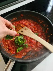 Hand streut Basilikum auf Tomatensauce