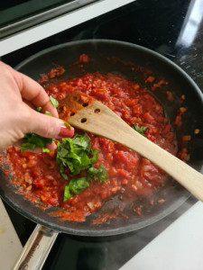 Hand streut Basilikum auf Tomatensauce