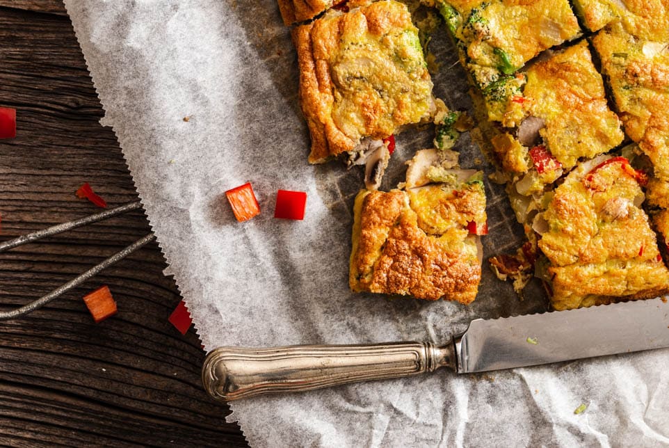 in Stücke geschnittene Frittata liegt auf Backpapier und daneben ein Messer
