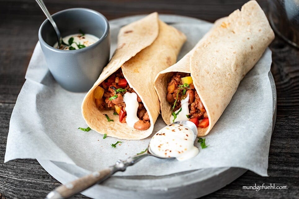 Two burritos filled with beef and beans are topped with sour cream