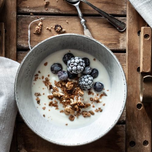 Eine Schüssel mit Granola, Brombeeren und Joghurt steht am Tisch