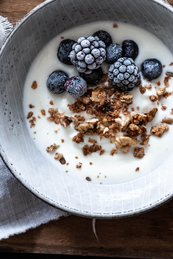 Eine Schüssel mit Granola, Brombeeren und Joghurt steht am Tisch