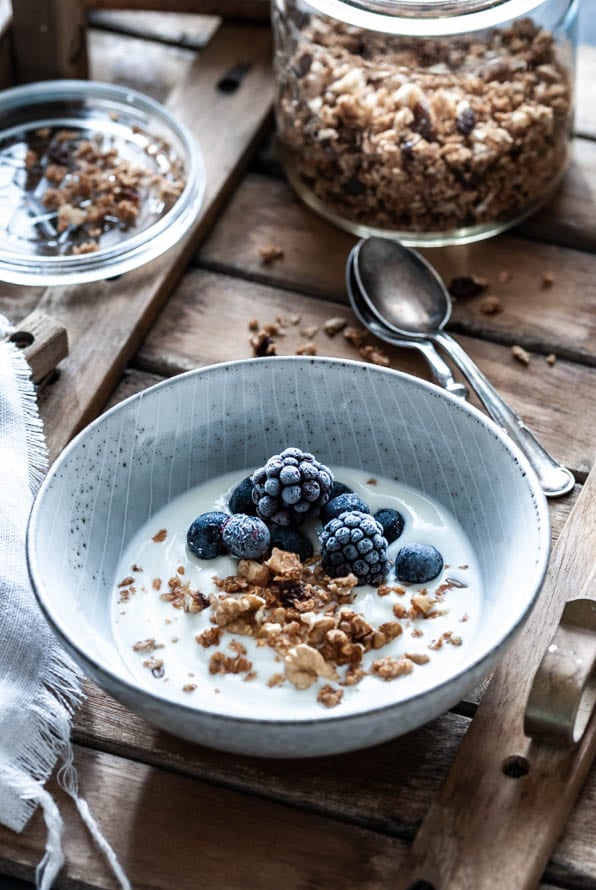 Eine Schüssel mit Granola, Brombeeren und Joghurt steht am Tisch
