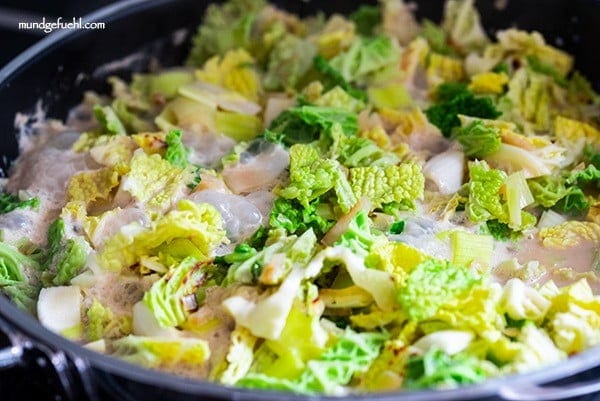 In einer Pfanne köchelt Huhn, Kohl und Lauch in cremiger Sauce