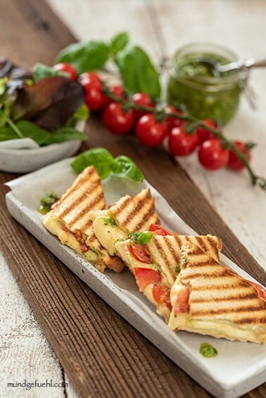 Toast with tomatoes, mozzarella and basil pesto is arranged in small triangles