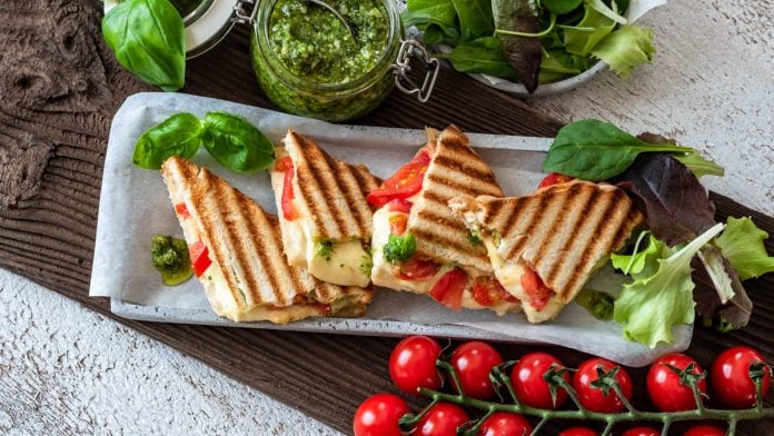 Toast mit Tomaten, Mozzarella und Basilikumpesto ist in kleinen Dreiecken angerichtet