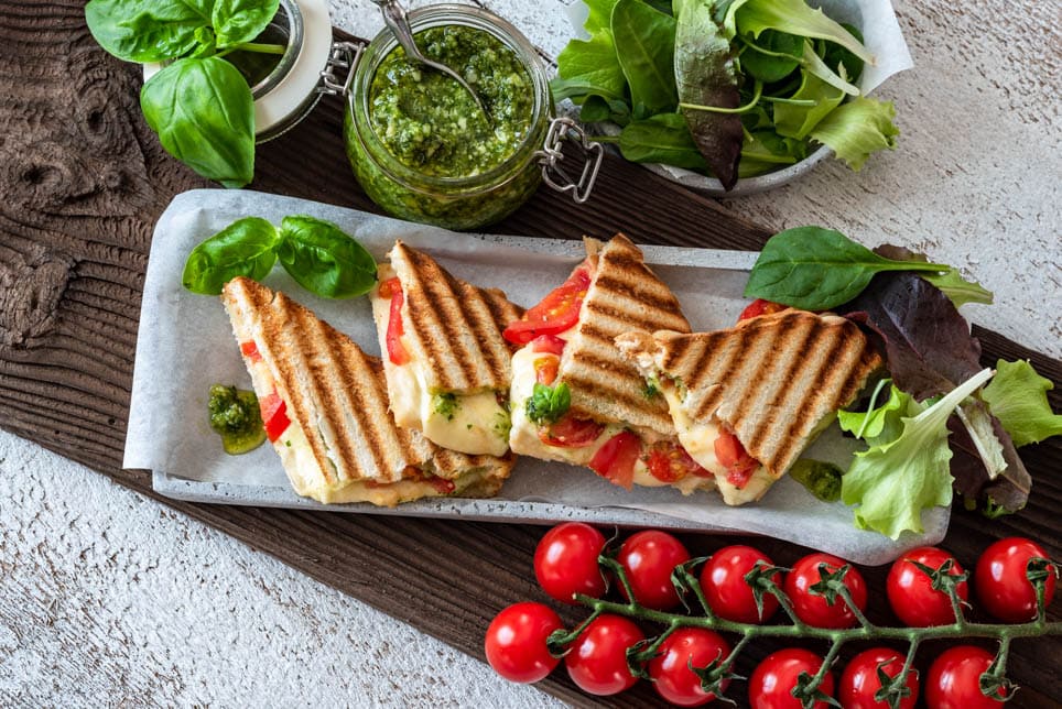 Toast mit Tomaten, Mozzarella und Basilikumpesto ist in kleinen Dreiecken angerichtet