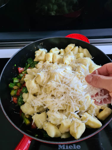Eine Hand streut Parmesan in Pfanne.