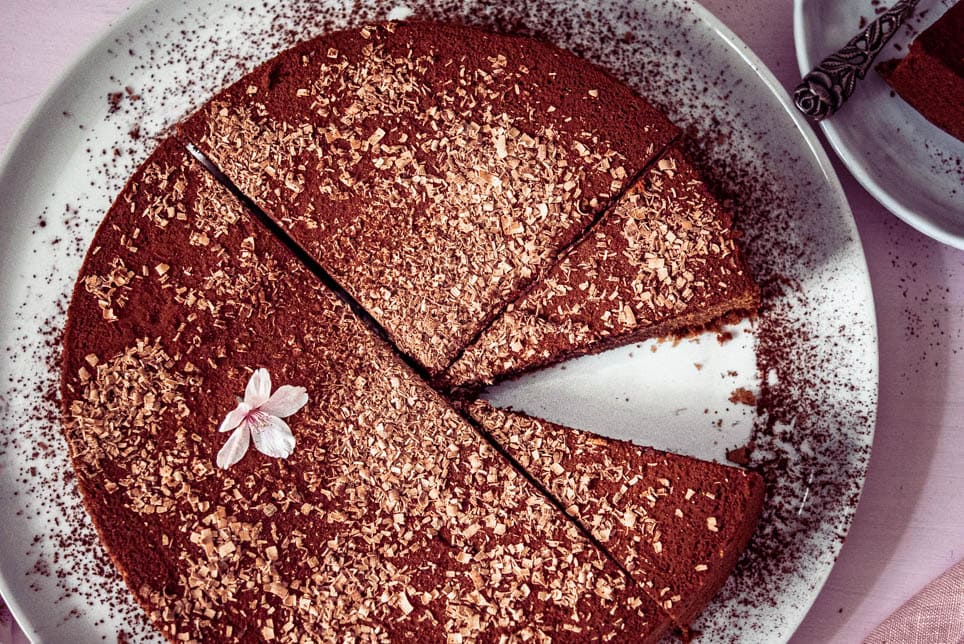 Eine Schokotorte garniert mit Blüten steht auf einem Tortenteller