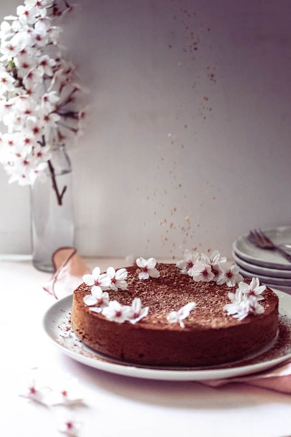 Schokostückchen fallen auf Schokotorte und Blumen stehen dahinter.
