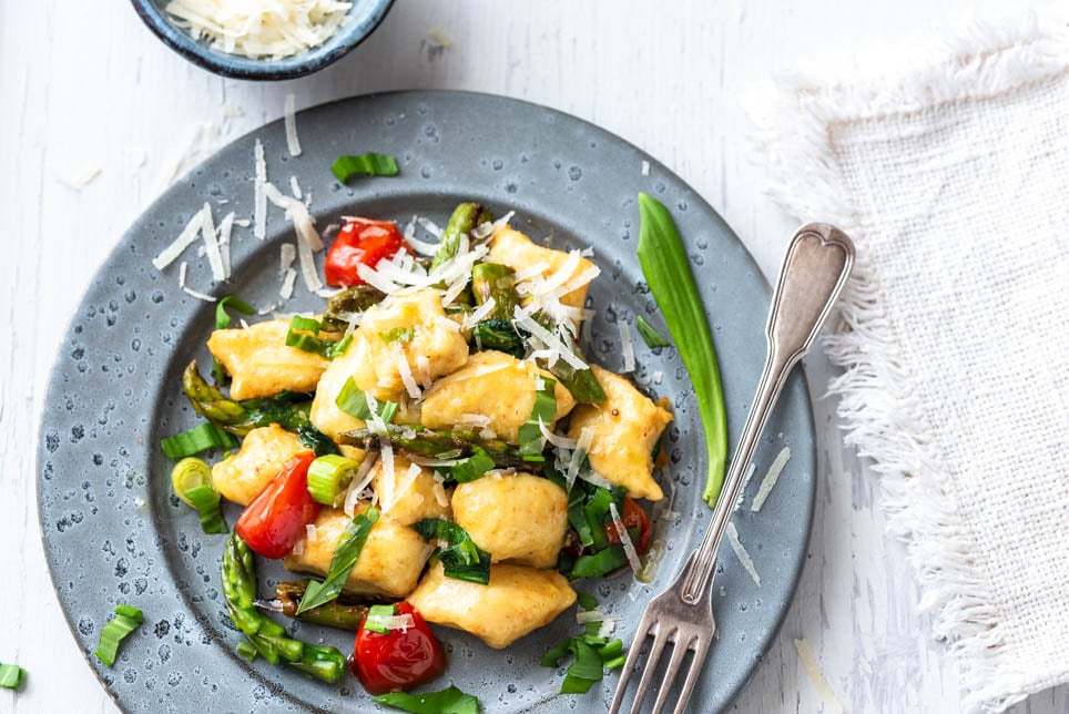 Ein Teller Gnocchi mit Spargel, Bärlauch und Tomaten mit Gabel.