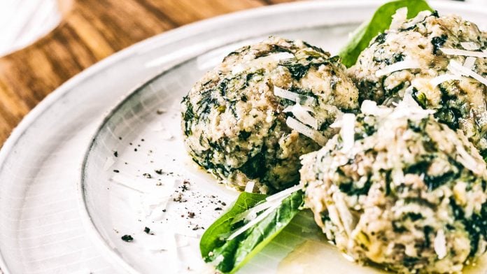 Spinatknödel mit zerlassener Butter, garniert mit Parmesan und Spinatblättern