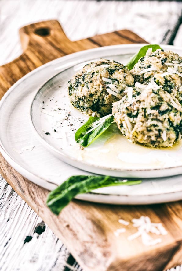 Spinatknödel mit zerlassener Butter, garniert mit Parmesan und Spinatblättern