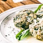 Spinatknödel mit zerlassener Butter, garniert mit Parmesan und Spinatblättern
