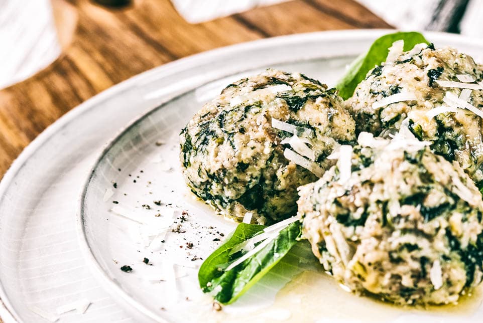 Spinatknödel mit zerlassener Butter, garniert mit Parmesan und Spinatblättern