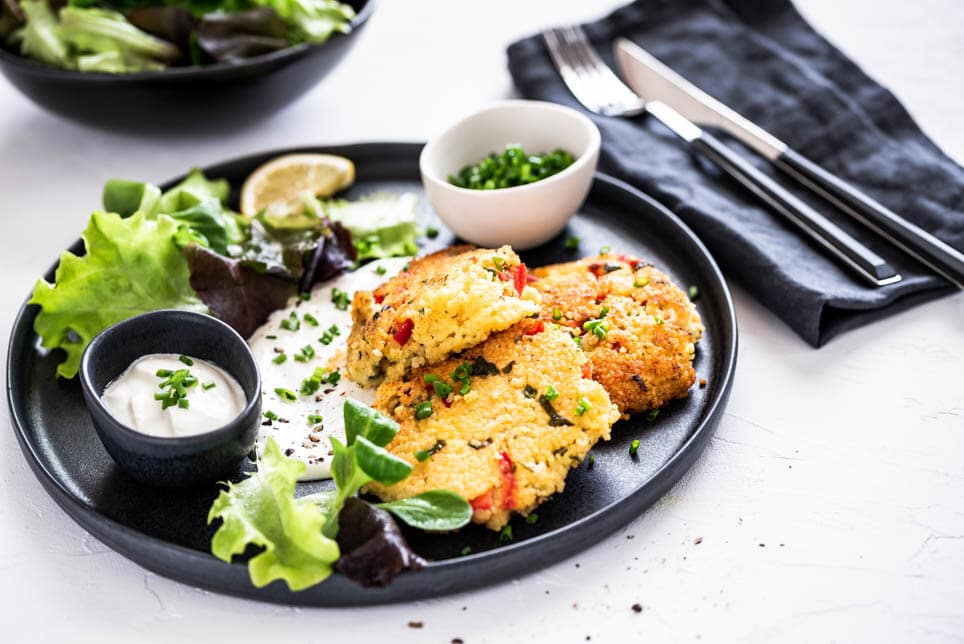 Knusprige Hirselaibchen mit Salat und Dip auf einem schwarzen Teller