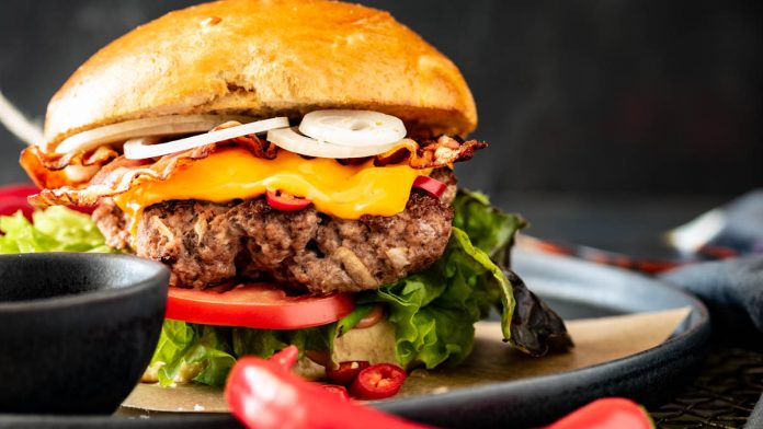 Ein Burger mit Rindfleisch, Zwiebeln und Salat wurde mit Sauce auf einem Teller angerichtet